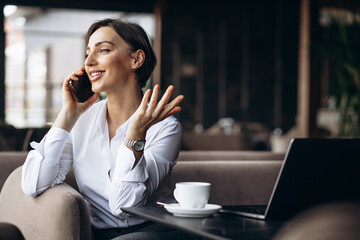 Business woman in a cafe working on laptop and using phone