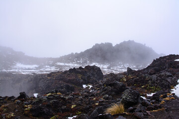 Snow storm building up over lava fields on the slopes of Mt Ruapehu. Patches of snow over Whakapapa Ski Field, Tongariro National Park, New Zealand
