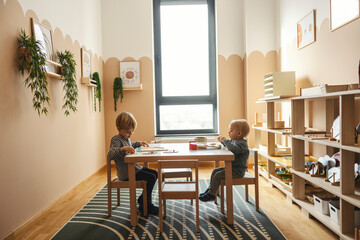 Two boys are sitting at the table and learning with use of educational toys in play room.