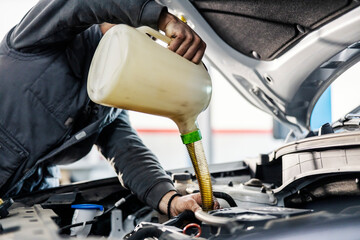 Cropped picture of a mechanic pouring oil in engine under the hood while working at mechanic's shop.