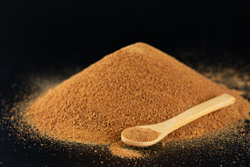 A pile with a wooden spoon with unrefined cane sugar Panela on a black.