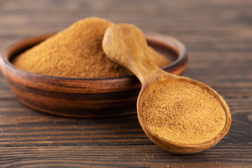Unrefined cane sugar Panela in a spoon and bowl on a wooden table.