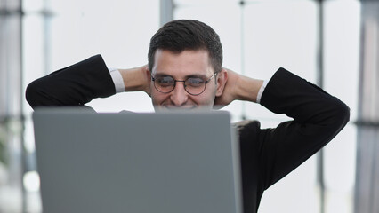 business man holding his hands behind his head while working on a laptop