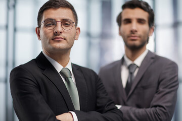 Two serious young businessmen standing with arms crossed in office