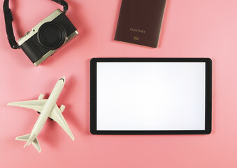 flat lay of digital tablet with blank white screen, airplane model, passport and digital camera isolated on pink background. travel planning concept.