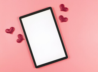 flat lay of digital tablet with blank white screen, red glitter hearts  isolated on pink background.