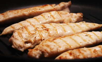 Pieces of chicken fillet are fried in a grill pan.