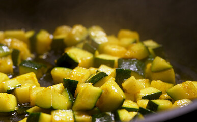Zucchini cubes are fried in a pan.