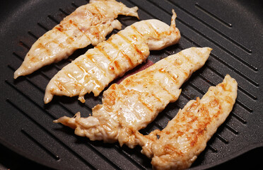 Pieces of chicken fillet are fried in a grill pan.