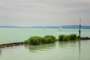 Obraz premium Scenic view of Lake Balaton in Hungary, summer landscape with green water, cozy settlement, yachts and sky, outdoor travel background