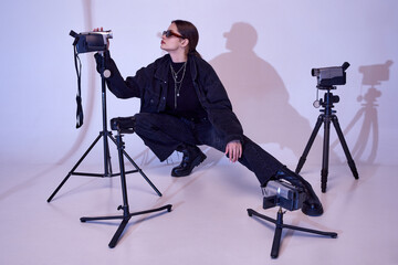 Photographer, video, content making. Beautiful young girl in stylish black clothes and trendy sunglasses posing over studio background. Concept of fashion, 80s, 90s style, retro and vintage, gadgets