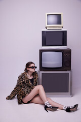 Influencer. Young girl in stylish animal print coat and trendy sunglasses posing near retro TV sets...