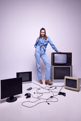 Young girl in jeans clothes posing around many retro TV sets and console. Game popularity, leisure...