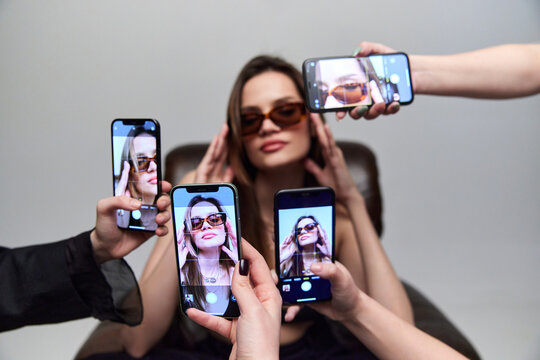 Beautiful young girl, social media influencer sitting, posing for mobile phone cameras taking photo. Concept of social media, popularity, fashion, beauty, 80s, 90s style, retro and vintage, gadgets - Powered by Adobe