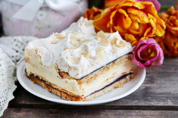 A slice of layer cake with red marmalade. Bouquet of flowers in the background.