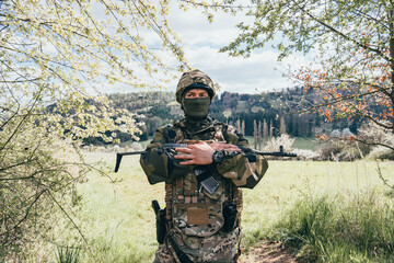 Fototapeta premium A member of a special unit. A soldier with an assault rifle in his hand and in uniform. Full tactical gear.A soldier in a forest in enemy territory