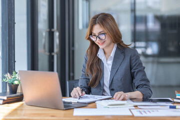 Asian Business woman using calculator and laptop at workplace doing math finance on an office desk,...