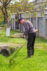 a man mows the grass with a chainsaw in the yard. the gardener is mowing grass with a string lawn mower.