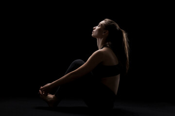 cute caucasian girl relaxing after yoga exercise against dark backgroung. side lit silhouette.