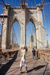 Asian female tourist wearing jacket, walking destination, happy to visit Brooklyn Bridge Landmark...