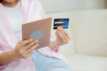 Hands of young asian woman sitting on sofa using digital tablet shopping online with credit card on couch, female paying with transaction financial, purchase and payment, business concept.