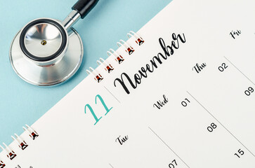 A November 2023 deskcalendar and medical stethoscope medical on blue background, schedule to check up healthy concepts.