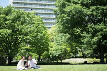 引っ越し先の新緑の公園でくつろぐ家族のイメージ　広角 © kapinon