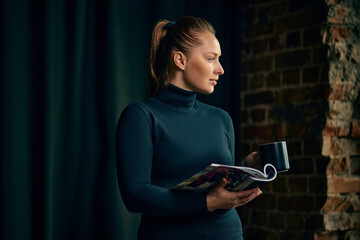 Confident, elegant business woman standing near window and looking through magazine. Staying in trends. Journalism. Concept of business, fashion, career development, profession, occupation