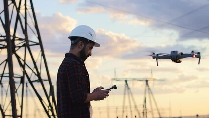 Man in a helmet controls uav using a remote control. Modern drone is flying towards the power plant with a check on the territory of the enterprise. Drone pilot engineer uav copter.