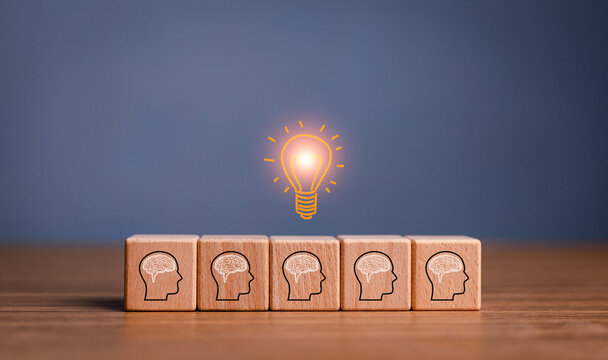 brainstorming creative idea and innovation. Hand putting over wooden cube block with light bulb icon on many people together having an idea symbolized by icons on cubes.