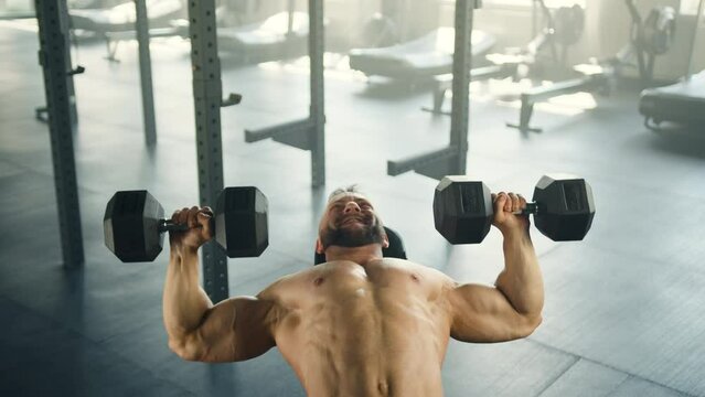 Medium shot of man with bare muscular torso doing dumbbell bench press in spacious light gym. Treadmills, air bikes, elliptical trainer in the background. High quality 4k footage Generative AI
