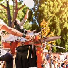 Summer music festival at the park. Music band playing on the stage. The drummer plays while the singer raises his fist in a successful pose