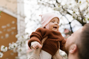 A father lifts up his daughter up in the air while they have fun together in the garden. 