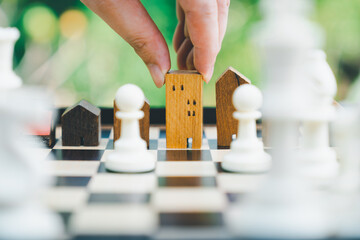 Hand of business man moving chess to Building and house models in chess game, competition success play. strategy, management or leadership concept	