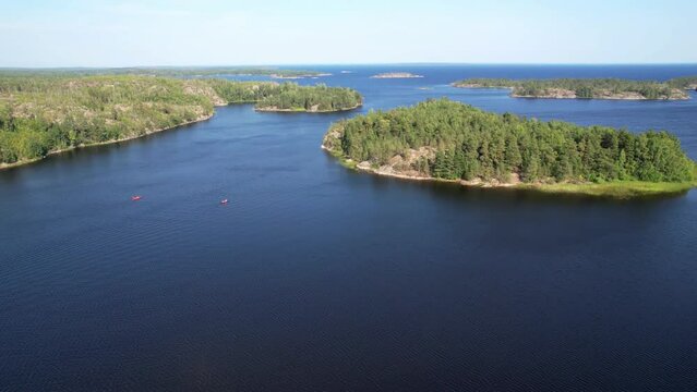 Aerial Drone Footage View: Flight over a rocky islands covered with a green coniferous forest. Two small orange kayaks on the water. Coastal zone of Lake Ladoga, Russia, Europe