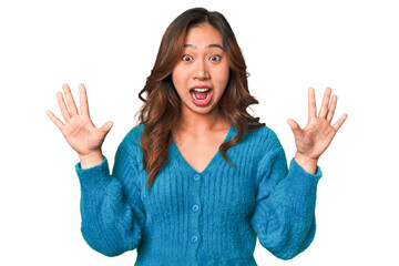 A young chinese woman receiving a pleasant surprise, excited and raising hands.