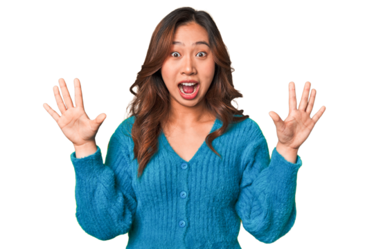 A young chinese woman receiving a pleasant surprise, excited and raising hands.