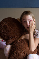 A young girl child crying while she cuddles her big teddy to comfort herself