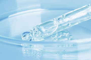 Transparent gel flowing from a pipette into a Petri dish. On a blue background. Close-up.