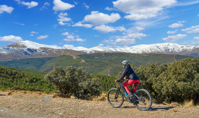 Fototapeta premium nice, active senior woman cycling with her electric mountain bike below the snow covered mountains of the Spanish Sierra Nevada, near Granada, Anslusia, Spain
