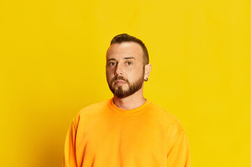 Portrait of bearded man with short hair, wearing sweatshirt and seriously looking at camera against...