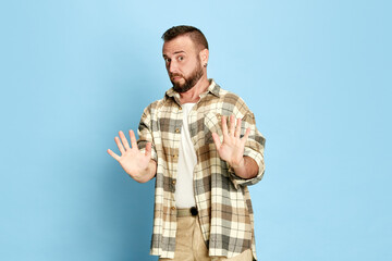 Decline. Portrait of bearded man in casual checkered shirt showing gesture of rejections, posing against blue studio background. Concept of human emotions, lifestyle, facial expression. Ad
