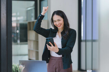 A businesswoman celebrates with her arms up while looking a smartphone in a happy and successful pose.