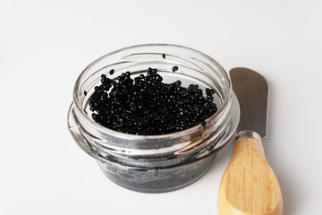 Fototapeta na wymiar black caviar in a glass jar and spatula on white glass