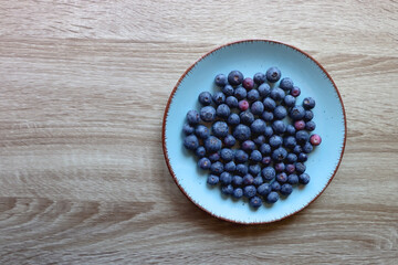 Turquoise plate with fresh blueberries on wooden background. Top view.