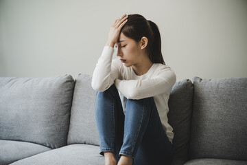 Unhappy anxiety young Asian woman covering her face with pillow on the cough in the living room at home.