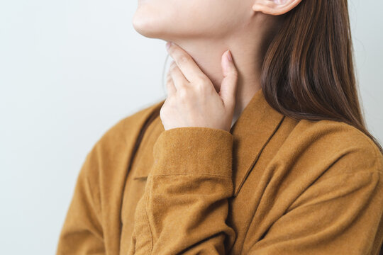 Sore throat in flu season. Young asian woman touching her neck and feeling pain in throat in the bedroom at home.