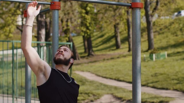 Athletic lebanese man in sportswear doing pull ups exercises on horizontal bar. Young guy pumping up back muscles on summer playground. Sports, health, fitness routine, workout. Strength, motivation