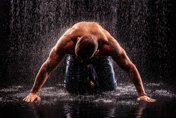 Athlete bodybuilder under jets of rain on a black background