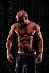 Athlete bodybuilder under jets of rain on a black background